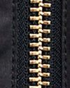 Close-up of a black zipper with gold-toned metal teeth on a dark textured fabric background.