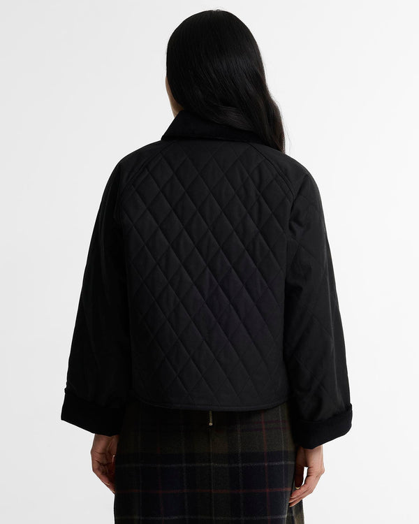 A model shown from the back wearing a black quilted cropped jacket with a high collar and a dark plaid skirt, against a plain white studio background.