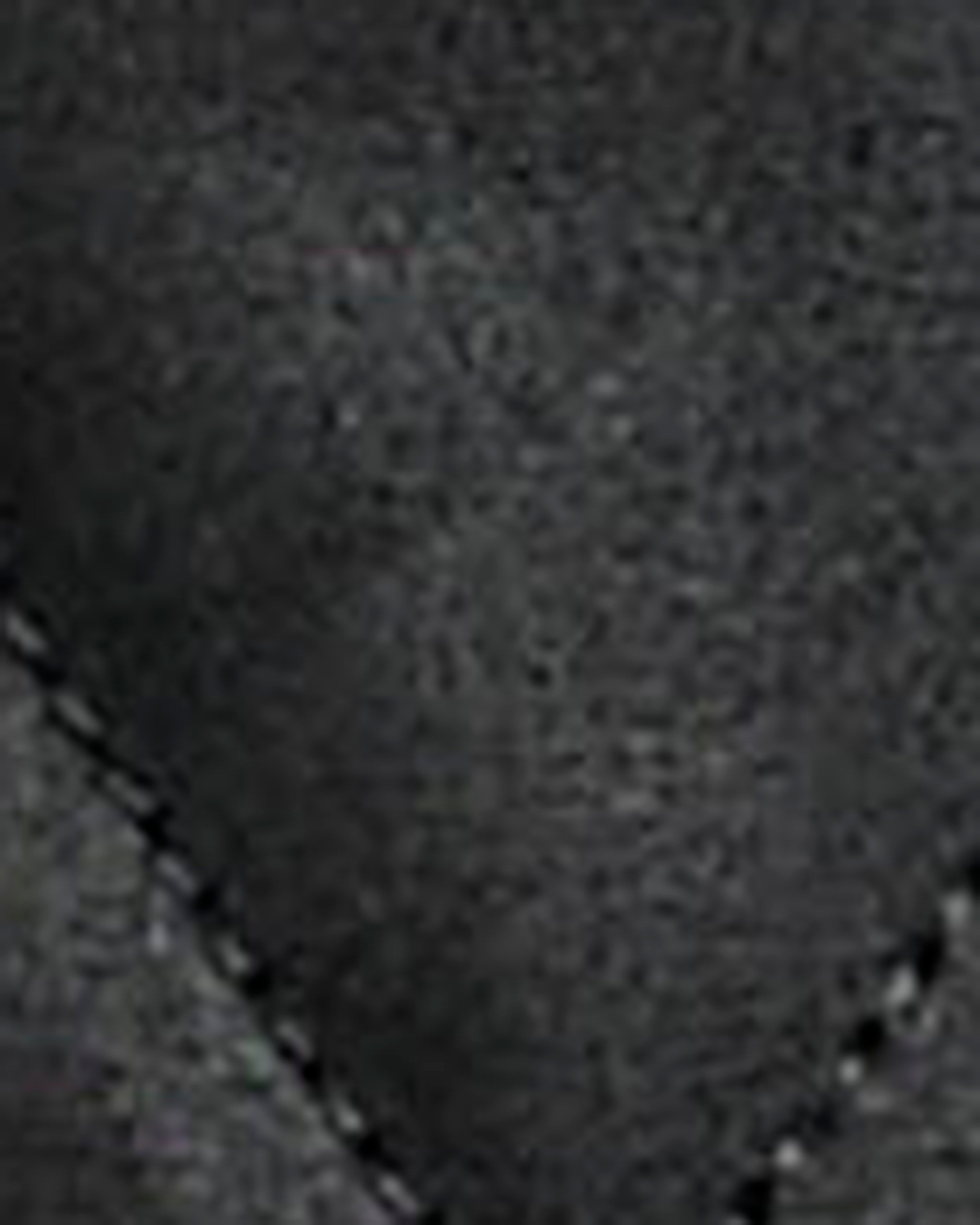A close-up texture shot of a dark gray fabric, showing a fine woven pattern and a diagonal stitched seam.