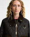 A close-up of a model wearing a dark olive diamond-quilted jacket with a contrasting dark brown corduroy collar and gold-tone hardware.