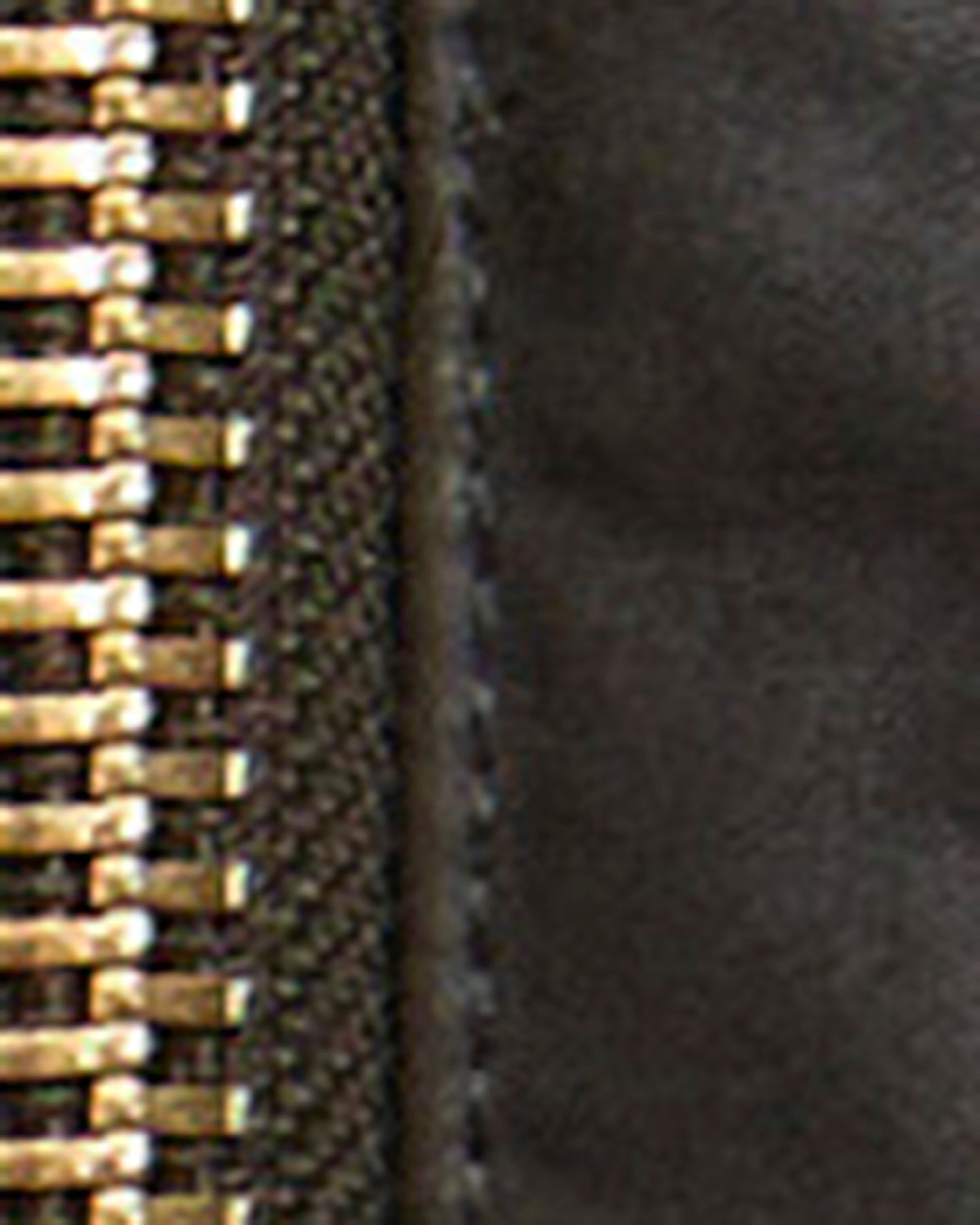 Close-up detail of a zipper with shiny gold-toned teeth and a dark textured fabric surface.