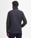 A man viewed from the back wearing a dark navy quilted puffer vest over a dark green knit sweater and dark blue jeans, against a plain white studio background.