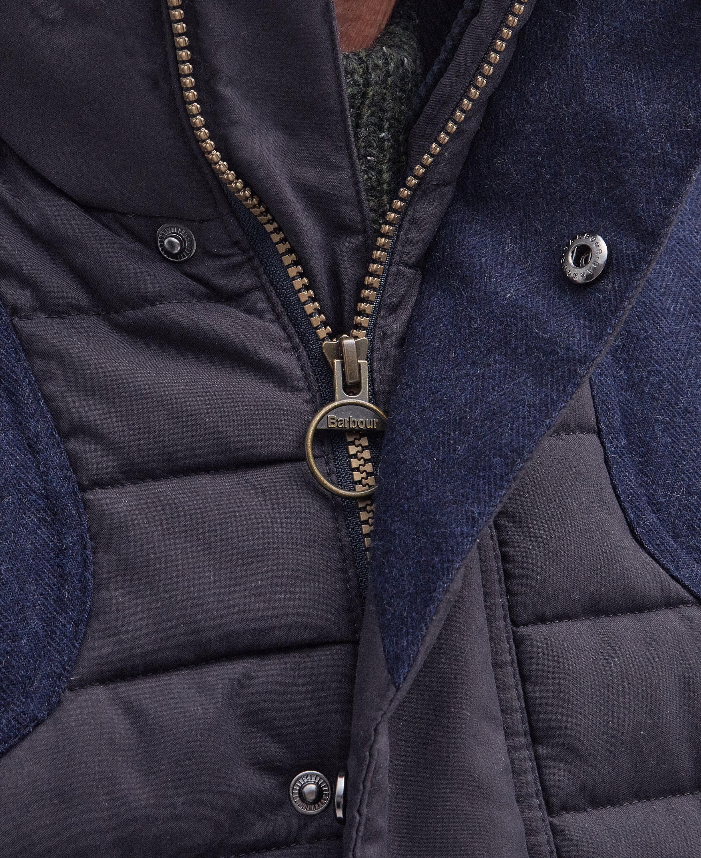 Close-up of a Barbour quilted vest with dark navy waxed cotton canvas, textured navy blue fabric panels, and a bronze-toned metal zipper with a circular ring pull.