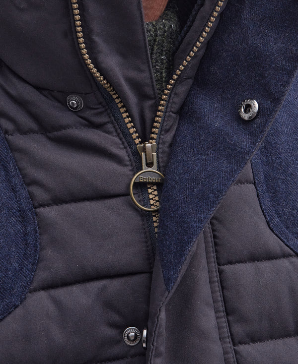 Close-up of a Barbour quilted vest with dark navy waxed cotton canvas, textured navy blue fabric panels, and a bronze-toned metal zipper with a circular ring pull.