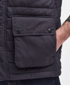 Close-up of a dark navy quilted puffer vest with a front flap pocket featuring snap buttons and an embossed Barbour logo, worn by a model.