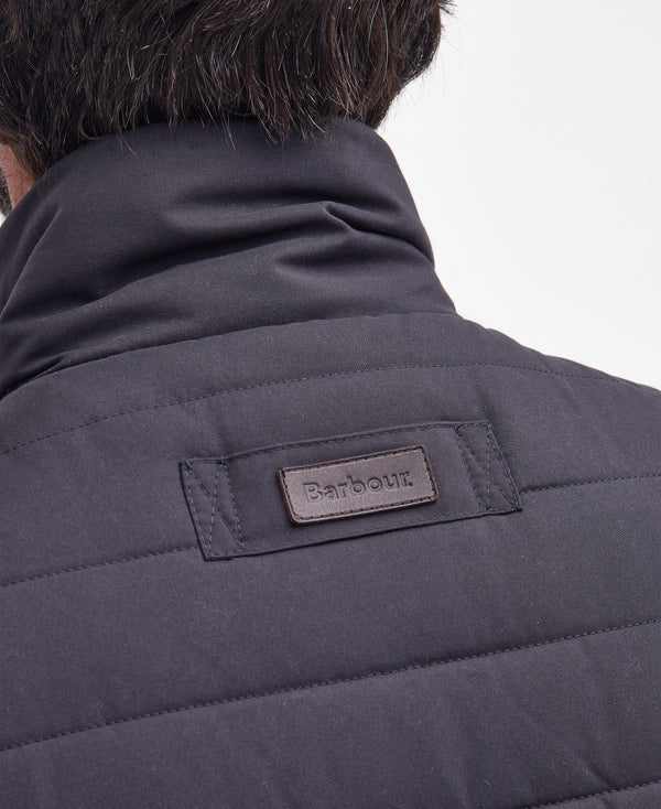 Close-up back view of a person wearing a dark navy quilted puffer jacket, showing a Barbour brand patch on the upper back.