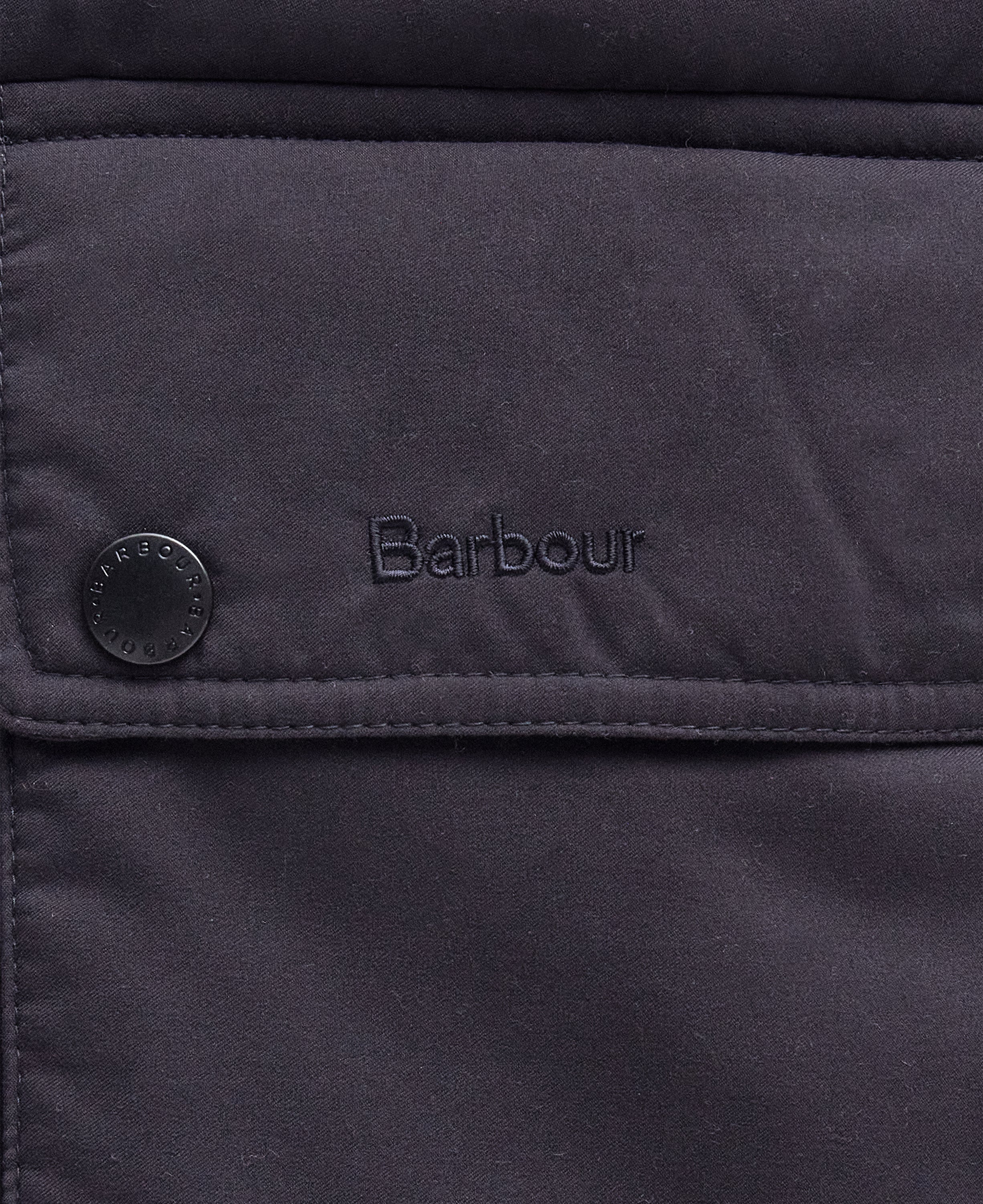 Close-up of a dark navy quilted fabric jacket with a flap pocket, a snap button, and the Barbour logo embroidered on the front.