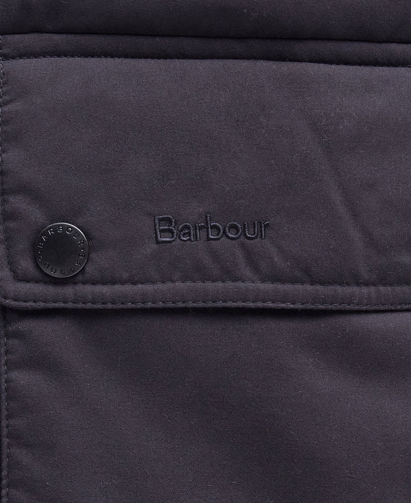 Close-up of a dark navy quilted fabric jacket with a flap pocket, a snap button, and the Barbour logo embroidered on the front.