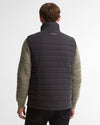 A man viewed from behind wearing a dark navy quilted puffer vest over a textured knit sweater, paired with dark jeans, against a light gray studio background.