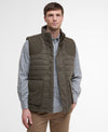 Man wearing a green quilted vest over a checkered shirt on a white background