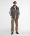 Man wearing a green puffer vest over a checkered shirt with brown pants on a white background