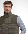 Man wearing a brown quilted vest over a checkered shirt on a white background