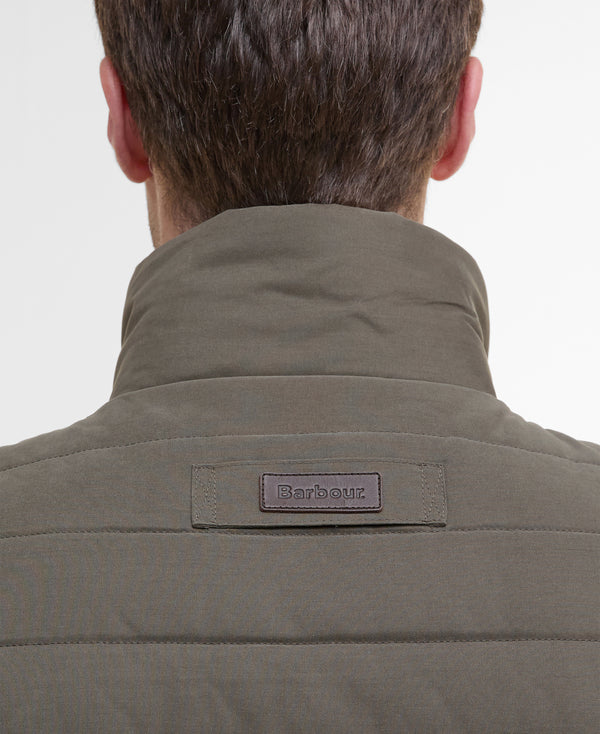 Close-up back view of a person wearing a quilted Barbour jacket in olive green, showing the high collar and the Barbour brand patch on the upper back.