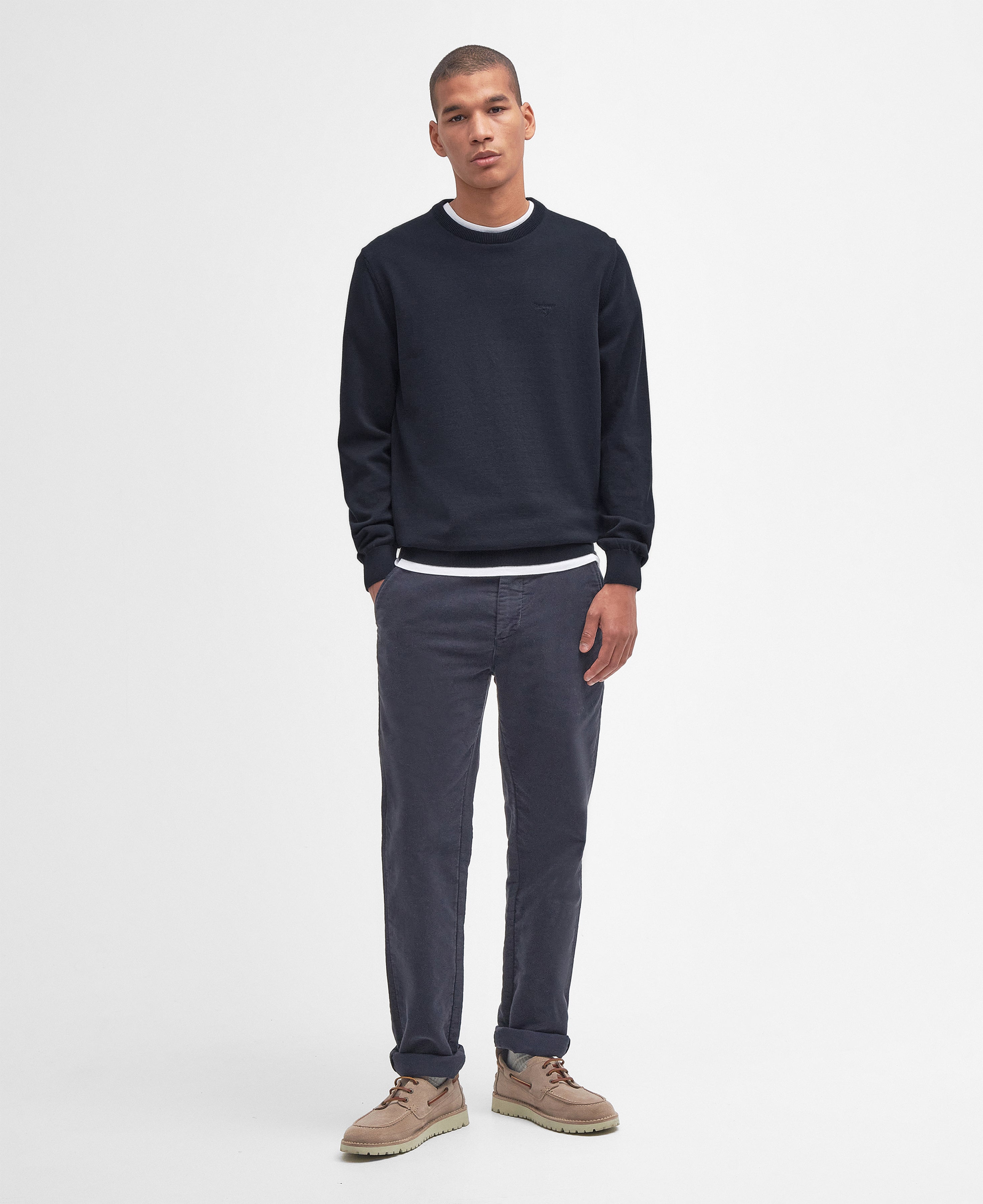 Man wearing a navy sweater and gray pants on a white background