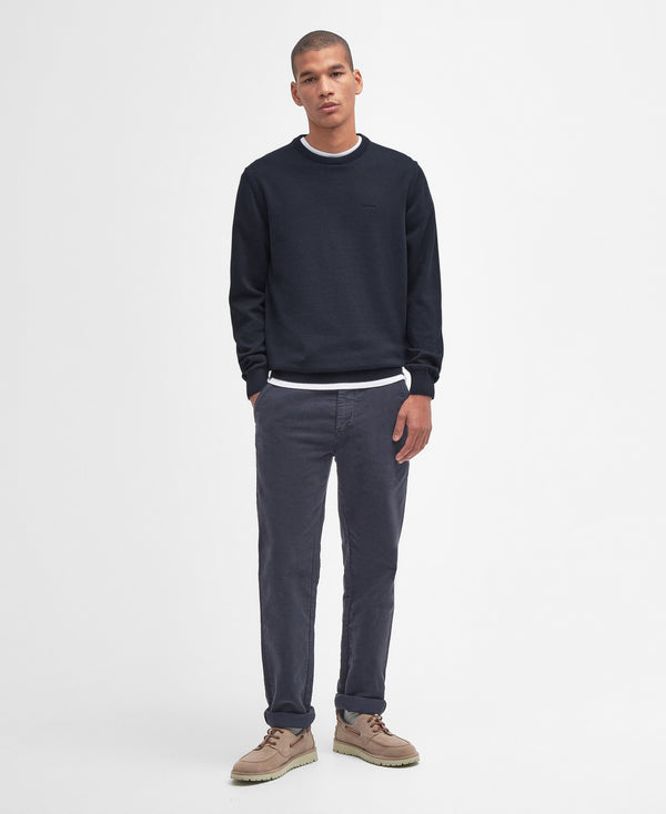 Man wearing a navy sweater and gray pants on a white background