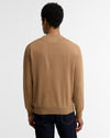 A man viewed from behind wearing a light brown crewneck sweater and dark blue jeans against a plain white background.