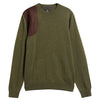 An olive green crewneck sweater with a contrasting dark brown suede patch on the right shoulder, displayed against a solid white background.
