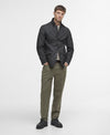 A man modeling a black quilted jacket, olive green trousers, and black shoes against a plain white studio background.