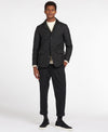 A man modeling a black utility jacket, dark charcoal trousers, a cream t-shirt, and black sneakers against a plain white studio background.