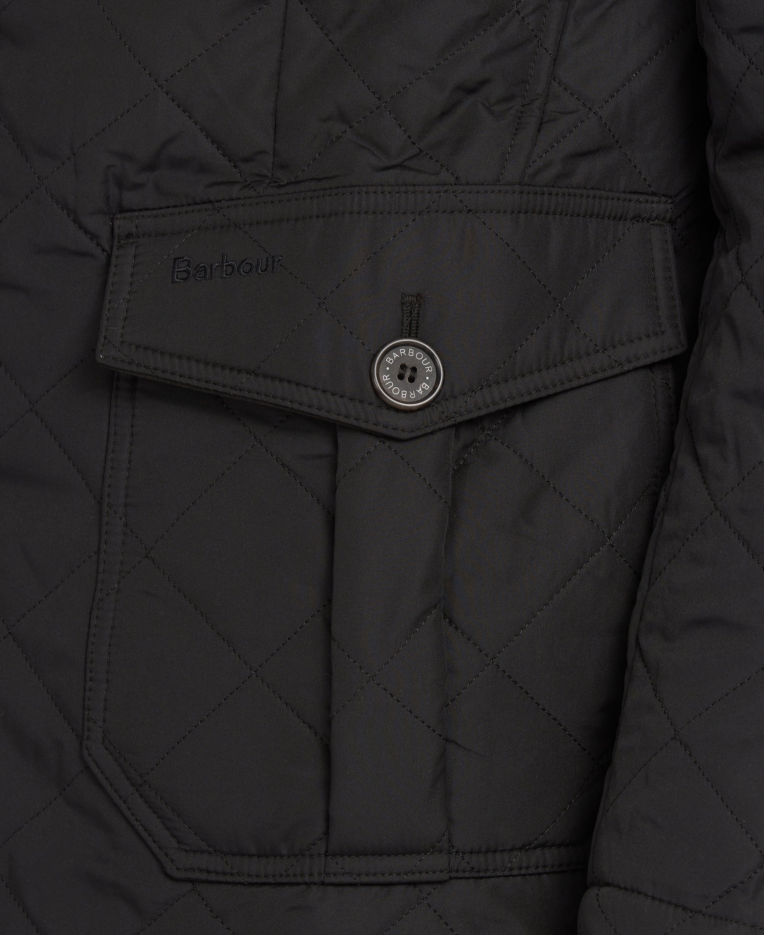 Close-up of a black quilted jacket with a diagonal flap pocket featuring a button and Barbour embroidery.