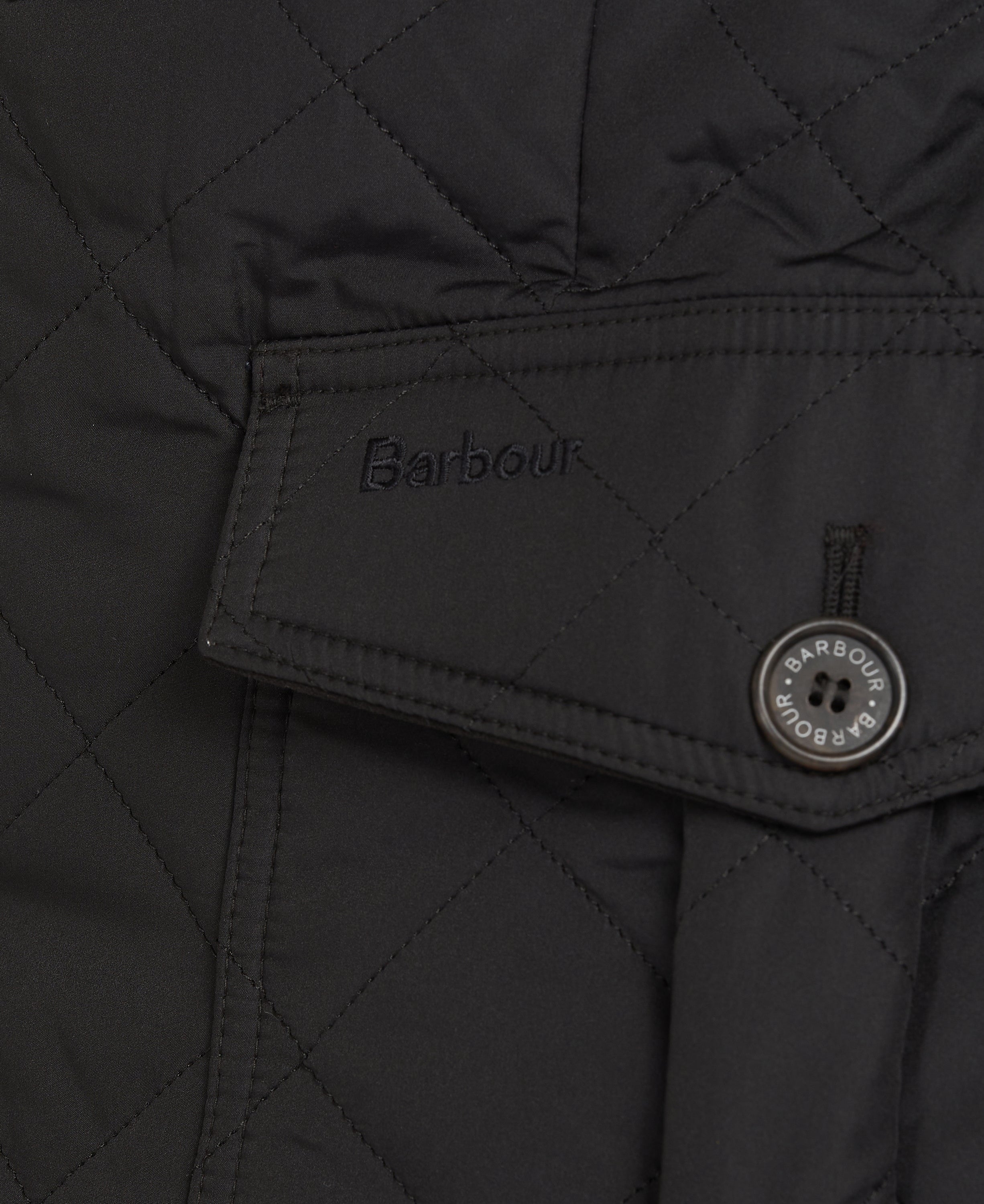 Close-up of a black quilted Barbour jacket showing a pocket flap with the Barbour logo and a round button.