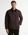 A man wearing a dark brown diamond-quilted jacket with a dark corduroy collar, photographed against a light gray studio background.