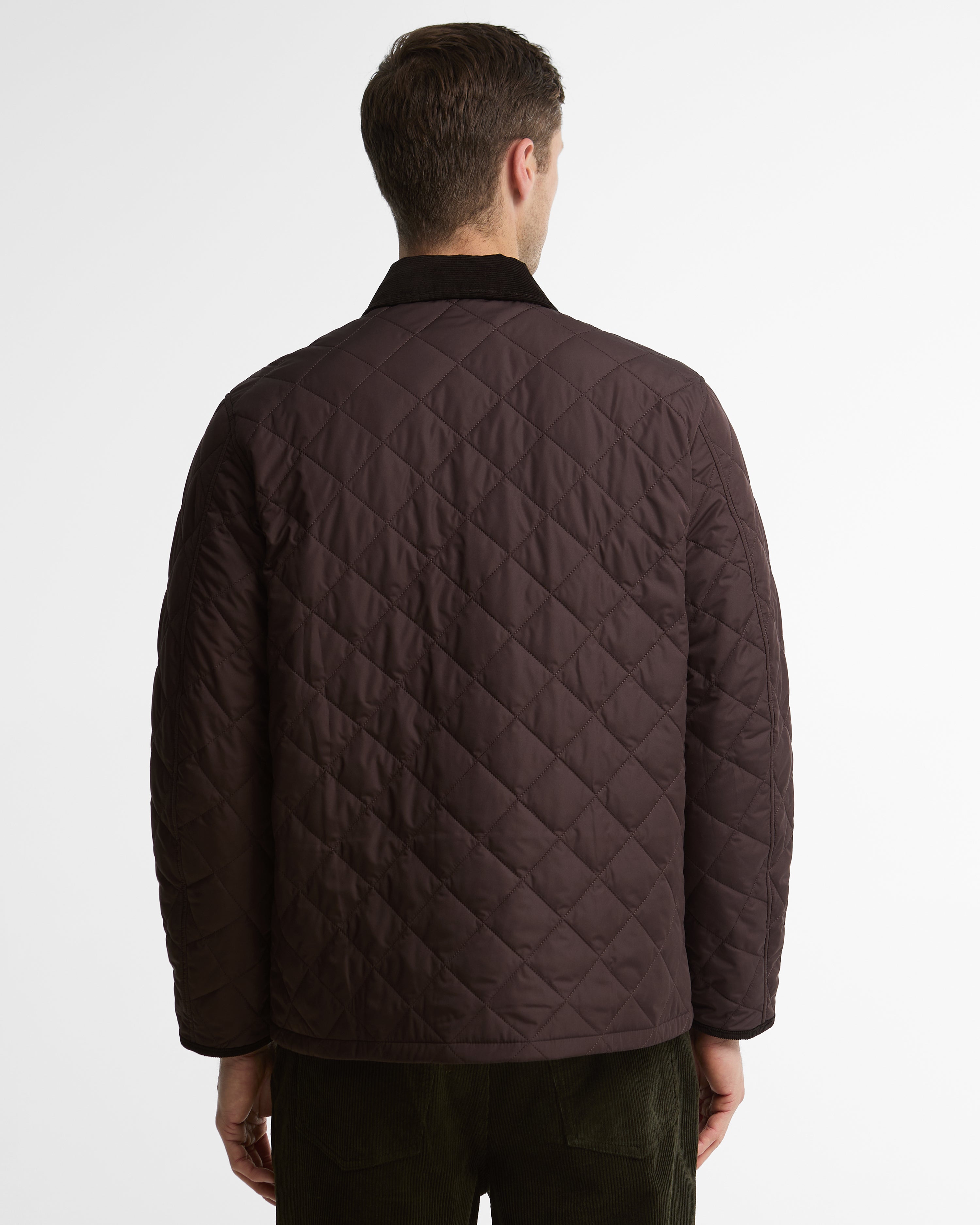 A man viewed from the back wearing a dark brown diamond-quilted jacket with a black collar, set against a plain light gray studio background.