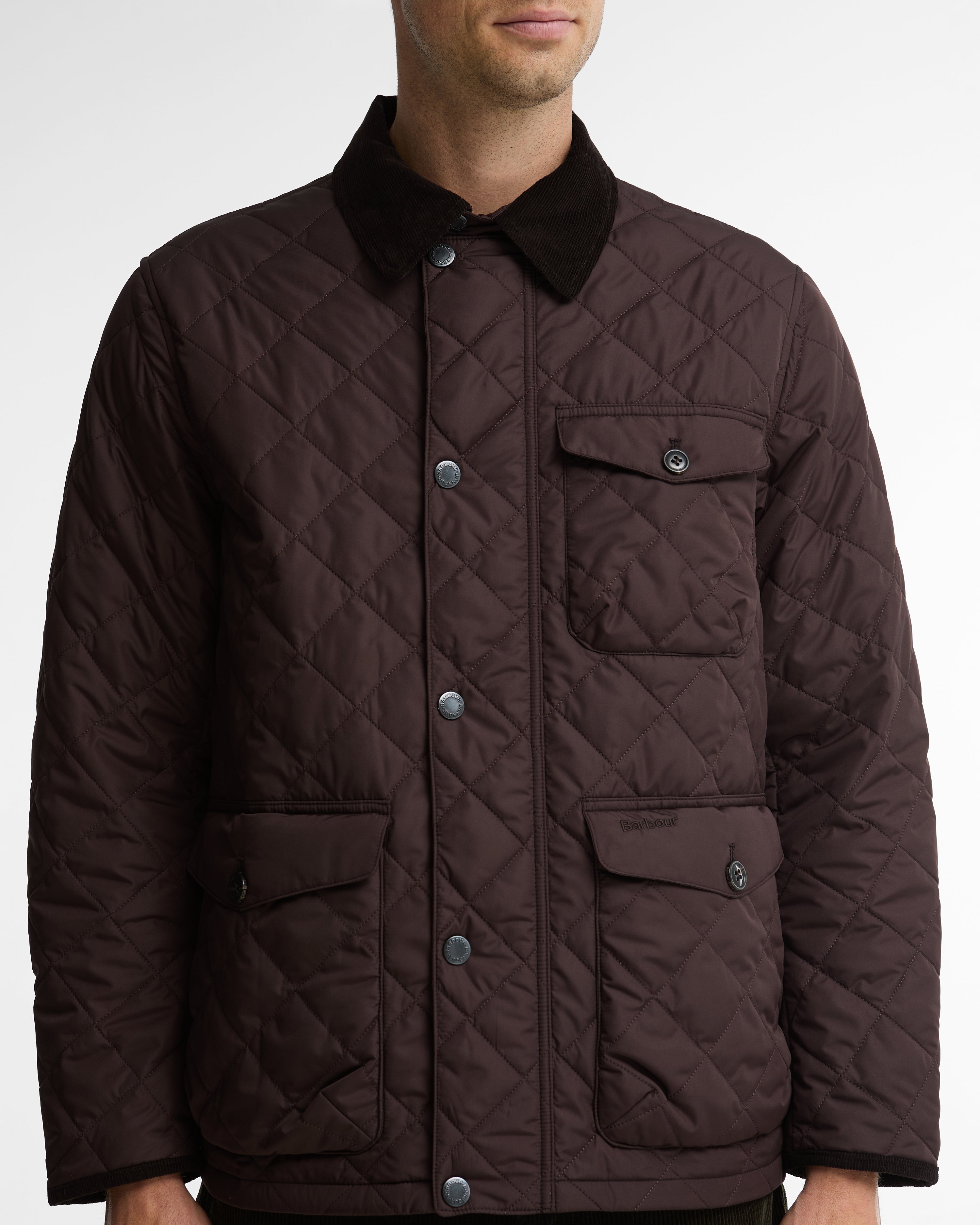 A man wearing a dark brown diamond-quilted jacket with a contrasting black corduroy collar and silver snap buttons, shown from the neck down against a light gray background.