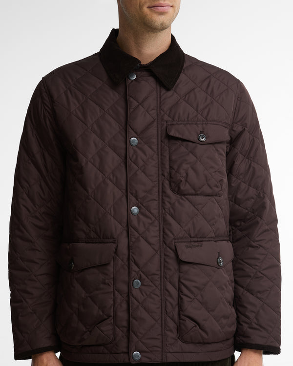 A man wearing a dark brown diamond-quilted jacket with a contrasting black corduroy collar and silver snap buttons, shown from the neck down against a light gray background.