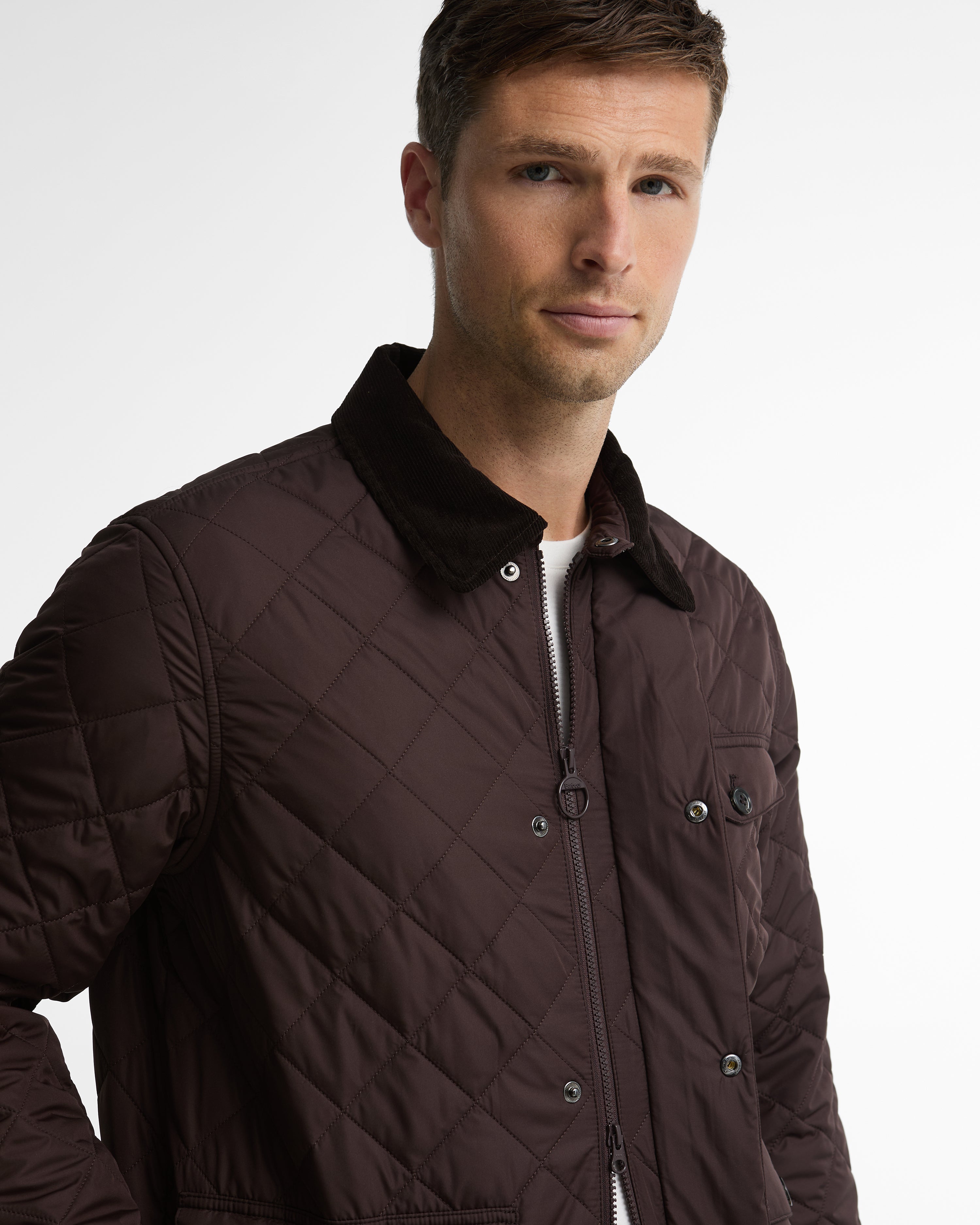 A man wearing a dark brown diamond-quilted jacket with a dark corduroy collar, photographed against a clean white studio background.