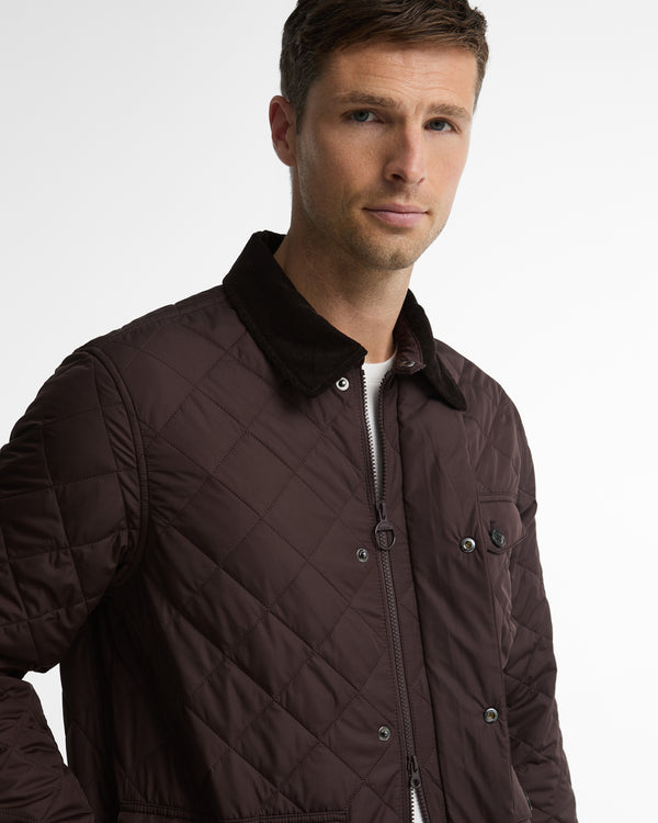 A man wearing a dark brown diamond-quilted jacket with a dark corduroy collar, photographed against a clean white studio background.
