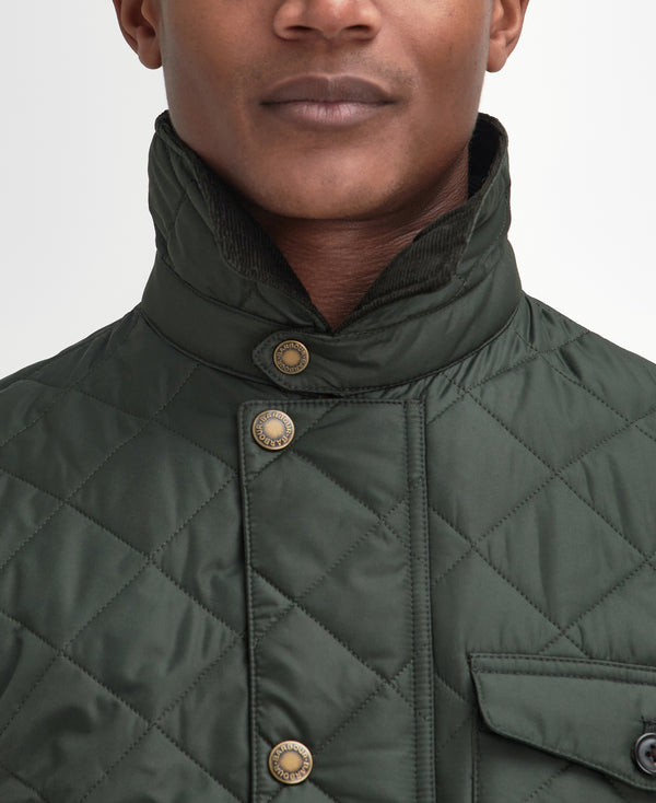Close-up of a man wearing a dark olive green quilted jacket with a high stand-up collar and brass snap buttons.