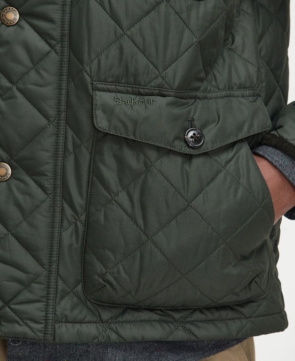 Close-up of a quilted Barbour jacket in dark olive green, showing a diamond-quilted pattern, a front flap pocket with a button, and part of a person's hand in the pocket.