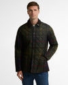A man wearing a dark green quilted plaid jacket with red and yellow lines, paired with blue jeans, photographed against a light gray studio background.