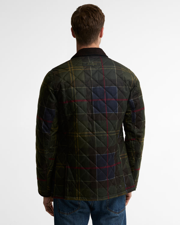 A man viewed from behind wearing a dark green quilted plaid jacket with blue, red, and yellow lines, paired with blue jeans, against a plain white background.