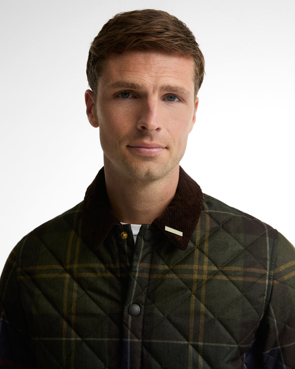 A man wearing a quilted plaid jacket with a dark brown corduroy collar, photographed against a plain light gray studio background.