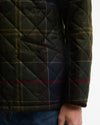 Close-up of a quilted Barbour jacket with a dark green and navy tartan pattern, featuring a diamond-quilted texture and a side pocket with the Barbour logo.
