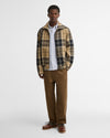A man modeling a Barbour Tartan Showerproof Blouson Jacket over a white button-down shirt, paired with brown trousers and brown shoes.