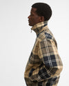 A man in profile wears a Barbour Tartan Showerproof Blouson Jacket in beige tartan, showing the stand-up collar and zip front.