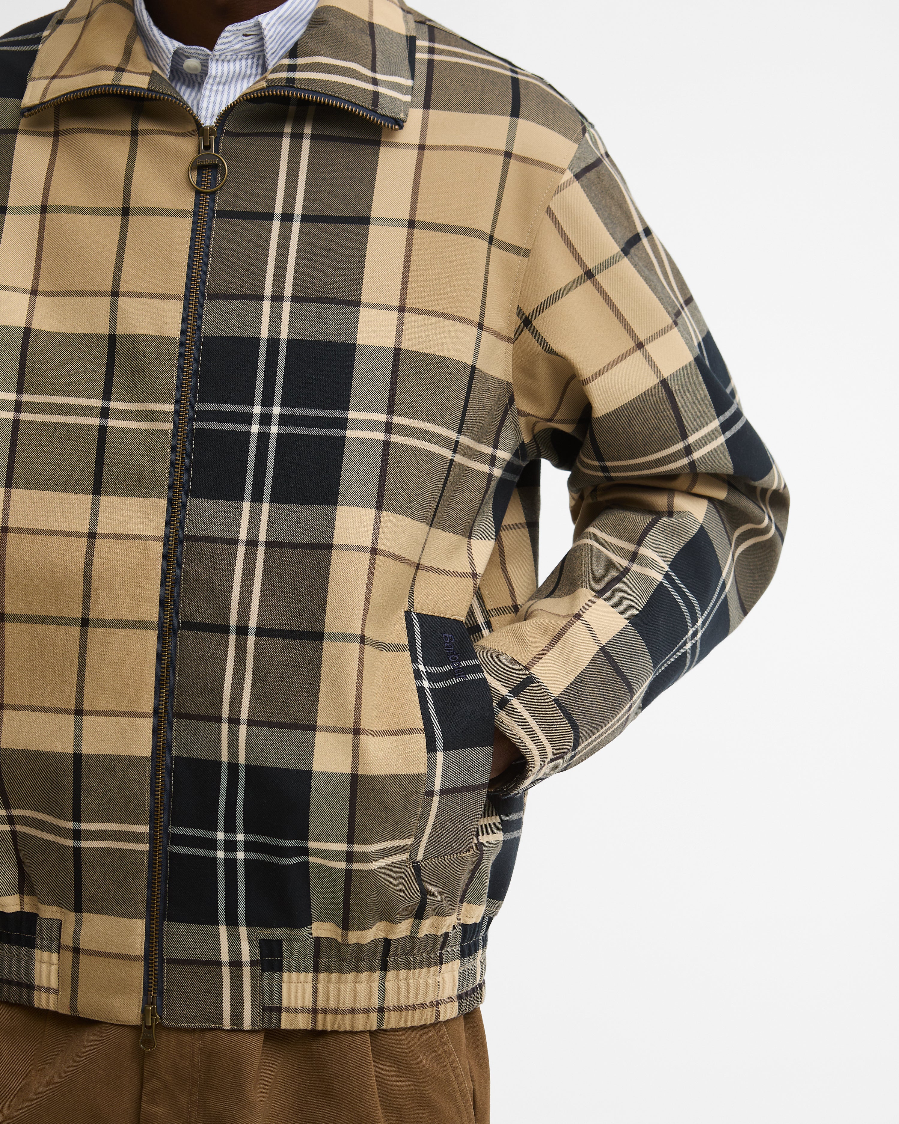 A close-up of a men's Barbour Tartan Showerproof Blouson Jacket, worn by a model. The jacket features a full-zip front, a stand-up collar, and side pockets.