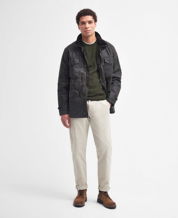 Model wearing the Barbour Sapper Wax Jacket styled for a complete outfit: green shirt, beige pants, and brown boots.