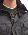 Close-up detail shot of the Barbour Sapper Wax Jacket with brass zipper and buttons, worn over a green shirt.