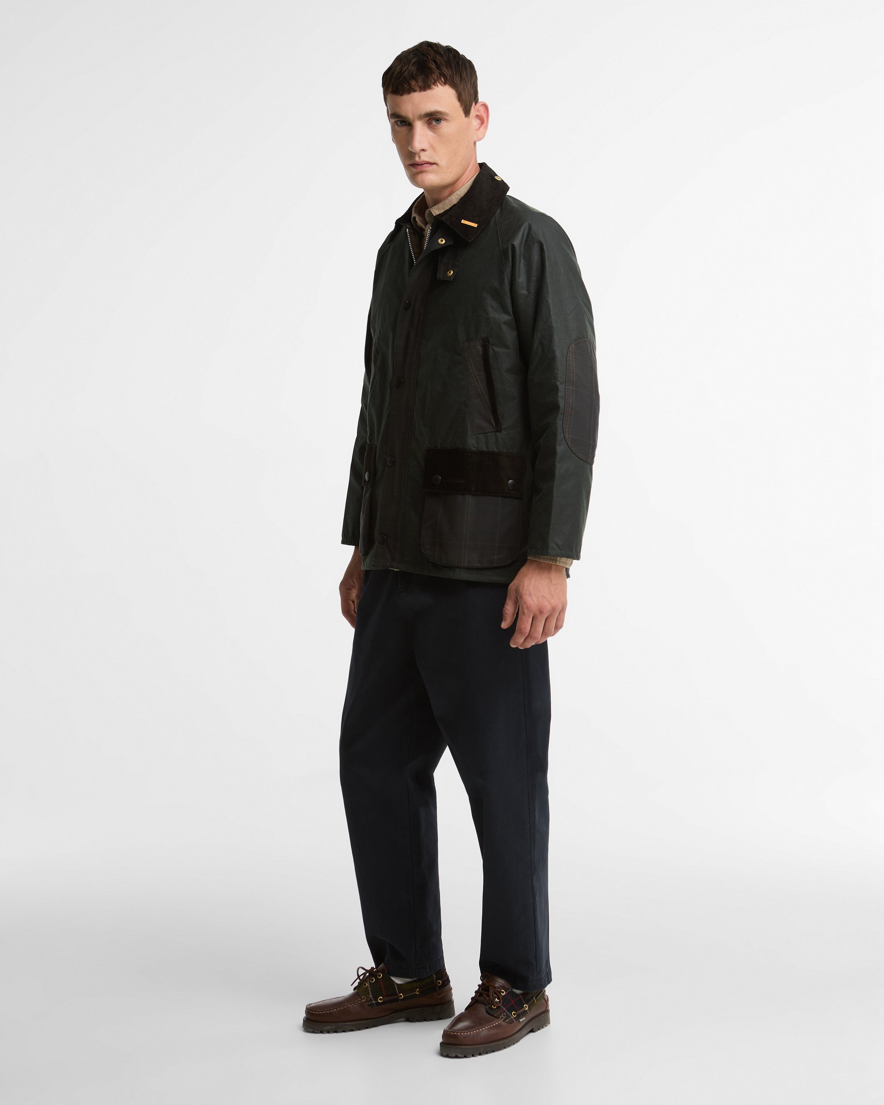 Model wearing the Barbour Icons Patch Bedale Wax Jacket in a three-quarter view, styled with navy trousers and brown leather boat shoes.