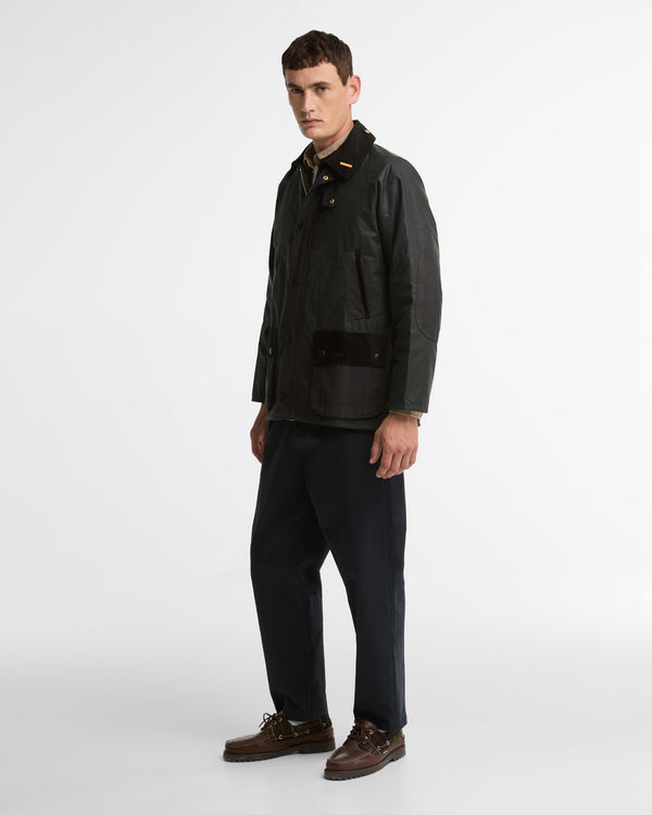 Model wearing the Barbour Icons Patch Bedale Wax Jacket in a three-quarter view, styled with navy trousers and brown leather boat shoes.