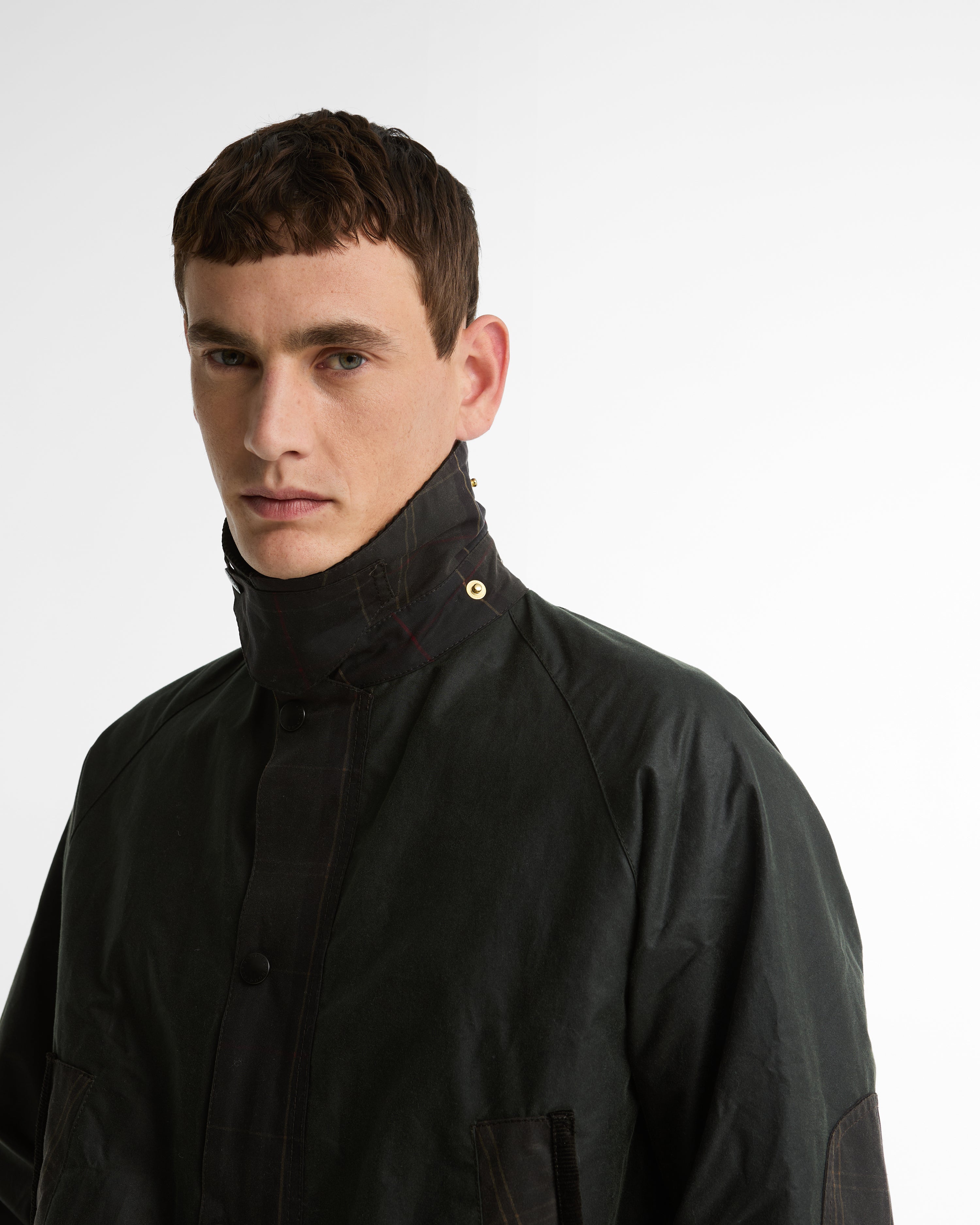 Close-up of a model wearing the Barbour Icons Patch Bedale Wax Jacket, showing the storm collar fastened with a gold snap button.