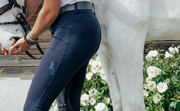 Woman in navy Struck breeches standing with her white horse.