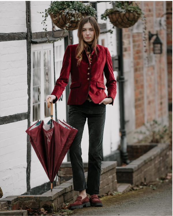 Woman in a red blazer holding a matching umbrella on a street.