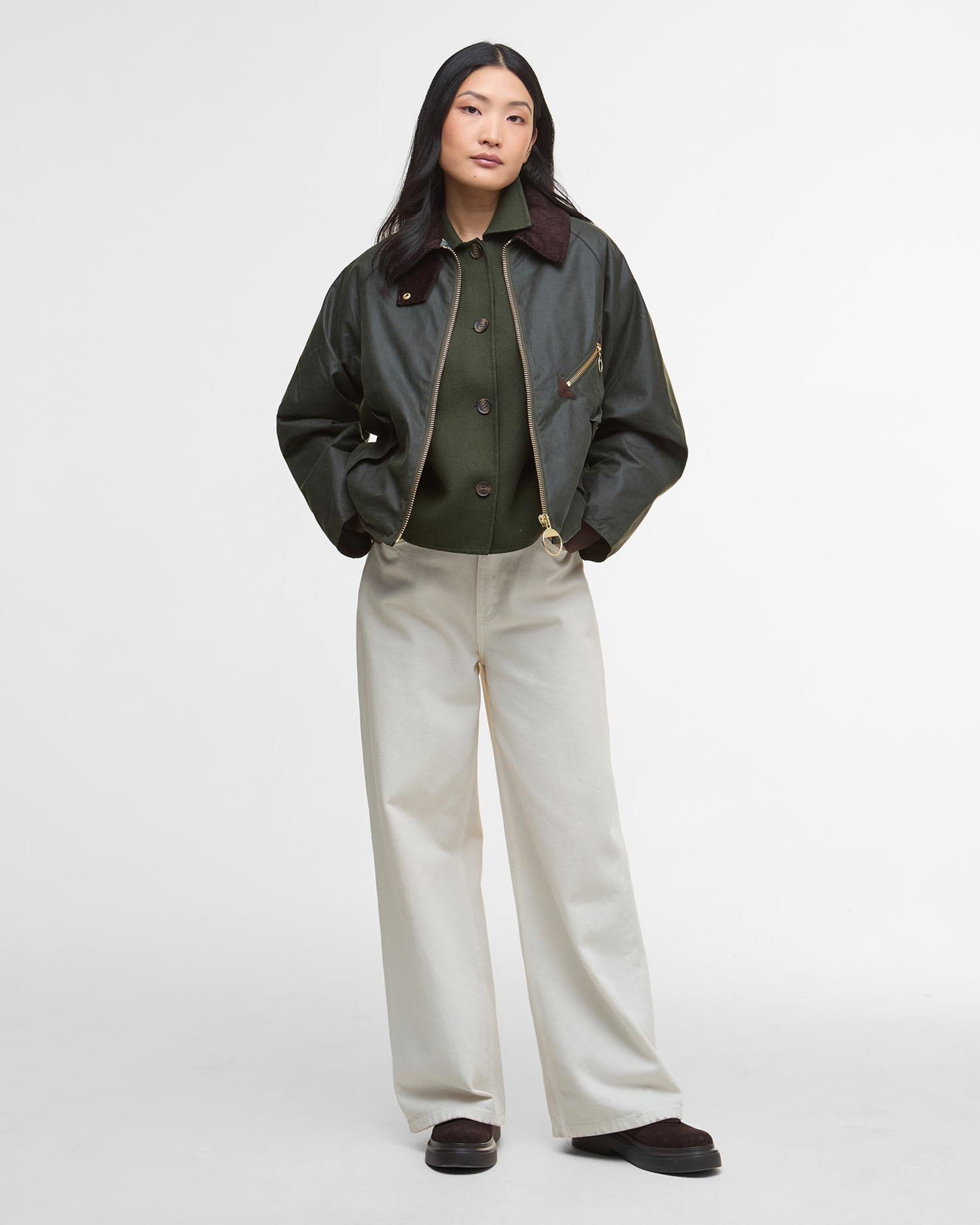 Person wearing a dark green jacket and light-colored pants on a white background