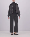 A video of a woman wearing a black Barbour waxed cotton jacket with gold buttons and a dark corduroy collar, posed against a light gray studio background.