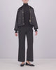 A video of a woman wearing a black Barbour waxed cotton jacket with gold buttons and a dark corduroy collar, posed against a light gray studio background.